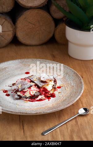 dessert francese millefoglie di pasta sfoglia e crema pasticcera e gelato su un piatto e su un tavolo di legno, primo piano. Foto Stock