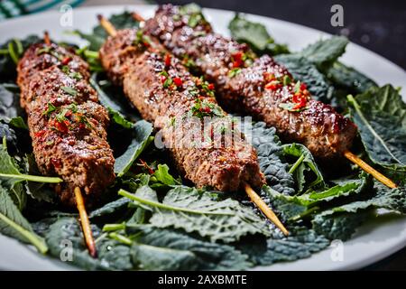 Succosa agnello kofta kebab di carne macinata con spezie cosparse di verdure tritate e peperoncino, servito su un letto di foglie di kale fresco su un piatto bianco su un Foto Stock