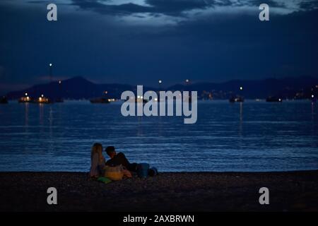 Sestri LEVANTE, ITALIA - 08 luglio 2017: Un paio di giovani che si trovano sulla spiaggia dopo il tramonto contemplando l'orizzonte Foto Stock