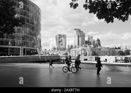 Pedoni sulla South Bank vicino al Municipio, Londra UK, guardando verso la Walkie Talkie Tower e la città Foto Stock