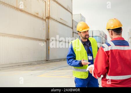 I lavoratori portuali che parlano vicino ai container di carico presso il soleggiato cantiere navale Foto Stock