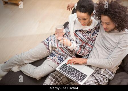 Affettuosa coppia in pigiama rilassante, utilizzando un computer portatile sul divano Foto Stock