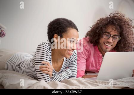 Coppia sorridente con notebook sul letto Foto Stock