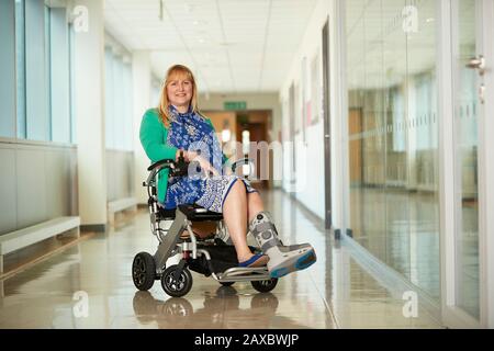 Ritratto donna sorridente indossando scarpe mediche in sedia a rotelle in corridoio Foto Stock