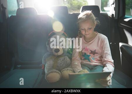 Ragazza con orsacchiotto con tablet digitale sul sedile posteriore dell'auto Foto Stock