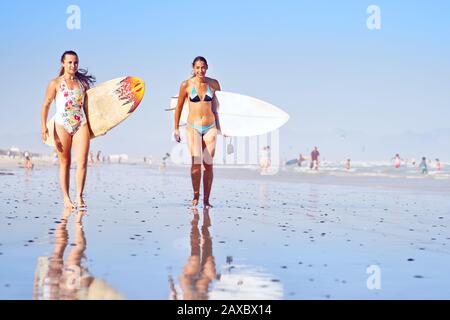 Ritratto sicuro giovani surfisti femmina sulla spiaggia soleggiata oceano Foto Stock