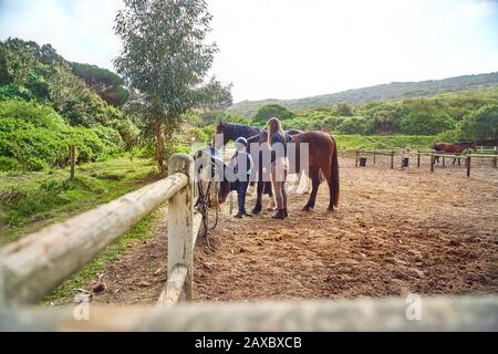 Istruttore femminile che insegna equitazione a ragazza in paddock rurale Foto Stock