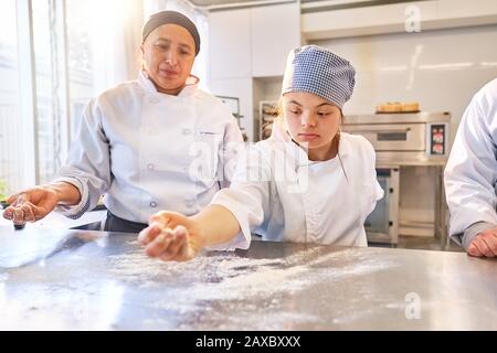 Giovane donna con La Superficie di flouring di sindrome Di Down nella classe di cottura Foto Stock