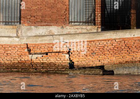 Un muro di mattoni rotto in acqua a Murano in una giornata di sole in inverno Foto Stock