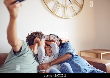 Affettuosa giovane famiglia incinta che prende selfie sul divano del soggiorno Foto Stock