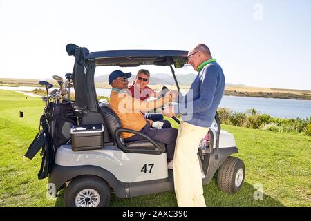 Gli amici del golfer maschio che parlano al golf cart sul campo soleggiato di golf Foto Stock