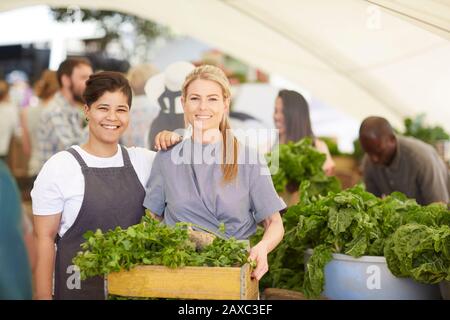 Ritratto donne sorridenti lavoratori con cassa di verdure al mercato contadino Foto Stock