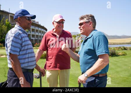 Amici golfer maschio felici che parlano sul campo da golf soleggiato Foto Stock