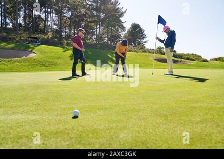 Gli amici del golfer maschio che mettono a casa sul campo da golf soleggiato Foto Stock