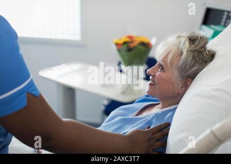 Infermiera femminile premurosa confortante donna anziana che riposa nel letto dell'ospedale Foto Stock