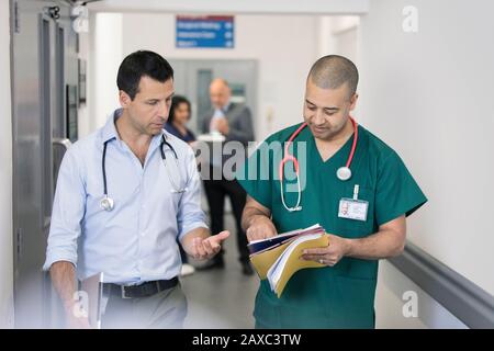 Medico e chirurgo di sesso maschile che discute la cartella medica, facendo giri nel corridoio dell'ospedale Foto Stock