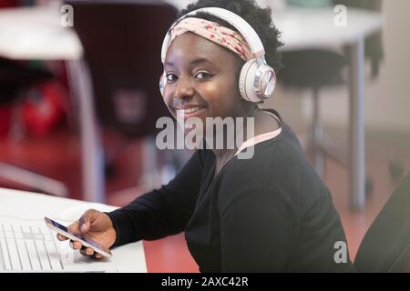 Ritratto sorridente, studente universitario sicuro con smart phone e cuffie in classe Foto Stock