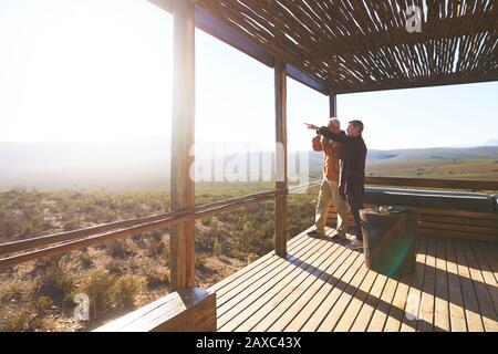 Coppia senior che guarda la vista soleggiata dal balcone Lodge safari Foto Stock