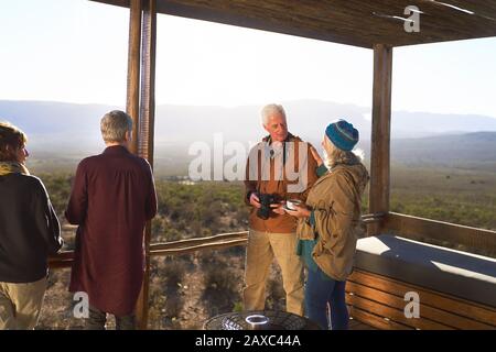 Coppia senior con macchina fotografica e tè sul soleggiato balcone Lodge safari Foto Stock