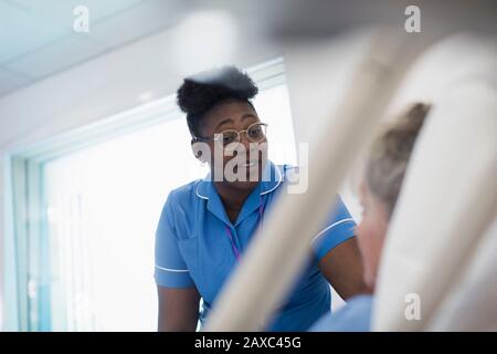 Infermiera di cura che parla con il paziente che riposa nel letto dell'ospedale Foto Stock