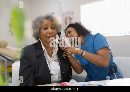 Medico femminile che esamina l'orecchio di pazienti anziani con otoscopio in ufficio medico Foto Stock