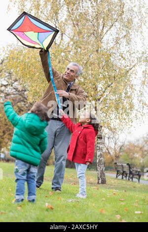 Nonno e nipoti che volano un aquilone nel parco autunnale Foto Stock
