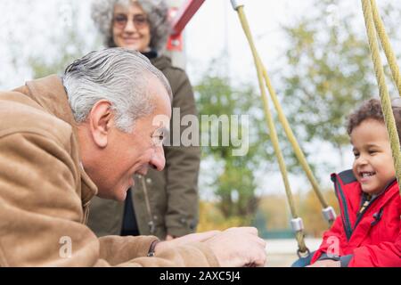 Nonno che gioca con il nipote in swing al parco giochi Foto Stock