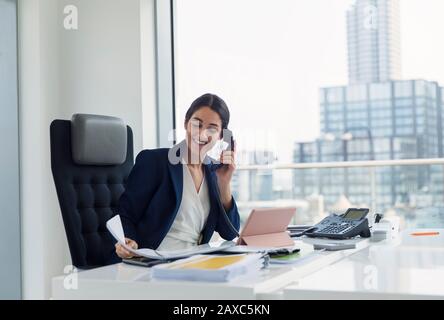 Donna d'affari sorridente che parla al telefono in ufficio urbano Foto Stock