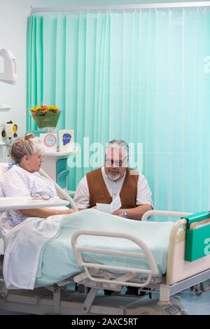 Uomo anziano con biglietto d'auguri per la visita della moglie che riposa nella stanza dell'ospedale Foto Stock