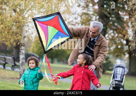 Nonno e nipoti che volano un aquilone nel parco autunnale Foto Stock