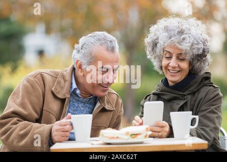 Coppia senior con smartphone, pranzo e caffè nel parco Foto Stock