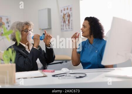 Medico femminile che insegna al paziente anziano come usare l'inalatore nell'ufficio del medico Foto Stock
