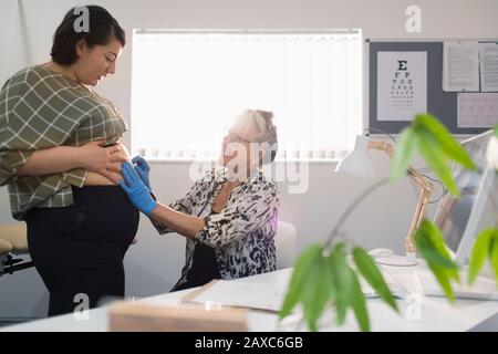 Medico femminile che esamina la paziente incinta in ufficio medico Foto Stock