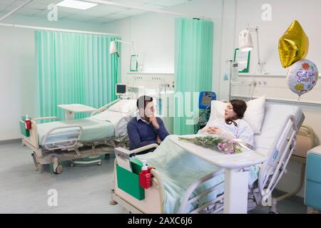 Uomo in visita, parlando con la moglie che riposa nel reparto dell'ospedale Foto Stock