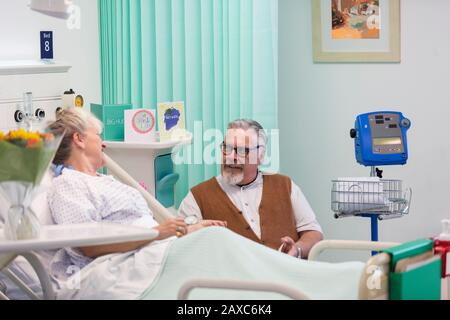 Affettuoso anziano che visita, parlando con la moglie che riposa nella stanza dell'ospedale Foto Stock