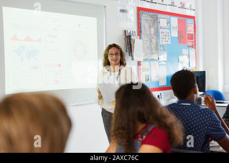 Insegnante femminile di scuola superiore che conduce la lezione allo schermo di proiezione in classe Foto Stock