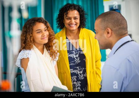 Pediatra maschile che parla con la ragazza paziente con braccio in imbracatura in sala esame Foto Stock