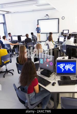 Giovani studenti di alto livello a computer che ascoltano l'insegnante a schermo di proiezione in classe Foto Stock