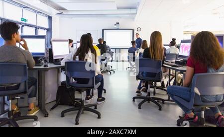 Giovani studenti di alto livello a computer che guardano l'insegnante a schermo di proiezione in classe Foto Stock