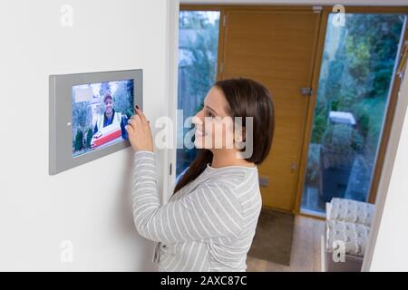 Donna sorridente che guarda il deliveryman che si avvicina alla porta anteriore dalla schermata di automazione domestica intelligente Foto Stock