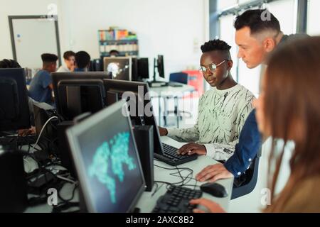 Un insegnante giovane e di alto livello che aiuta gli studenti di ragazzi a usare il computer in laboratorio Foto Stock