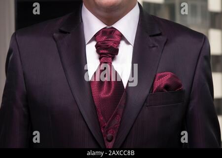 Traje de novio granate con caleco bordado y corbatón. Foto Stock