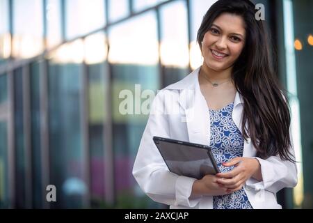 Bella donna indiana americana in un camice da laboratorio, veste bianca con tablet elettronico, medico professionista sorridente ritratto Foto Stock