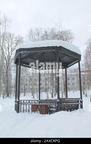 Gazebo in metallo aperto con panchine nel parco, coperto di neve in giornate nuvolose. Concetto di miglioramento e decorazione dell'ambiente urbano. Foto di scorta per Web, stampa, sfondo e sfondo. Foto Stock