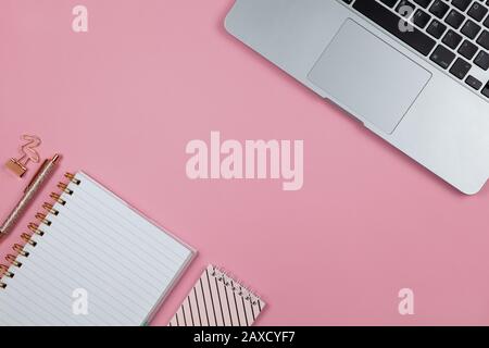 Moderno spazio di lavoro femminile, vista dall'alto. Laptop, notebook, penna in oro rosa, morsetto su sfondo rosa, spazio copia, piatto. Desktop di blogger, f Foto Stock