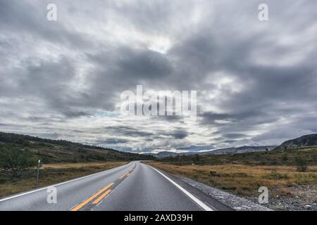 Strada di montagna guida in Norvegia. Epico cielo panoramico con vista sulle nuvole. Viaggiare in auto, turismo naturale. Drammatico cloudscape, colori vividi del nord, scansione Foto Stock