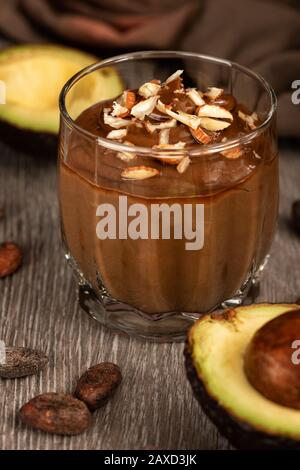 Dessert avocado con cacao in un bicchiere su una superficie di legno. Prodotti vegani crudi. Foto Stock