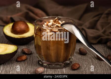 Сhocolate dessert con avocado in un bicchiere su una superficie di legno. Prodotti vegani crudi. Foto Stock