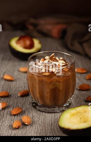 Сhocolate dessert con avocado in un bicchiere su una superficie di legno. Prodotti vegani crudi. Foto Stock