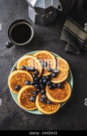 Dolci frittelle fatte in casa con caffè e mirtilli su vecchio tavolo da cucina. Vista dall'alto. Foto Stock